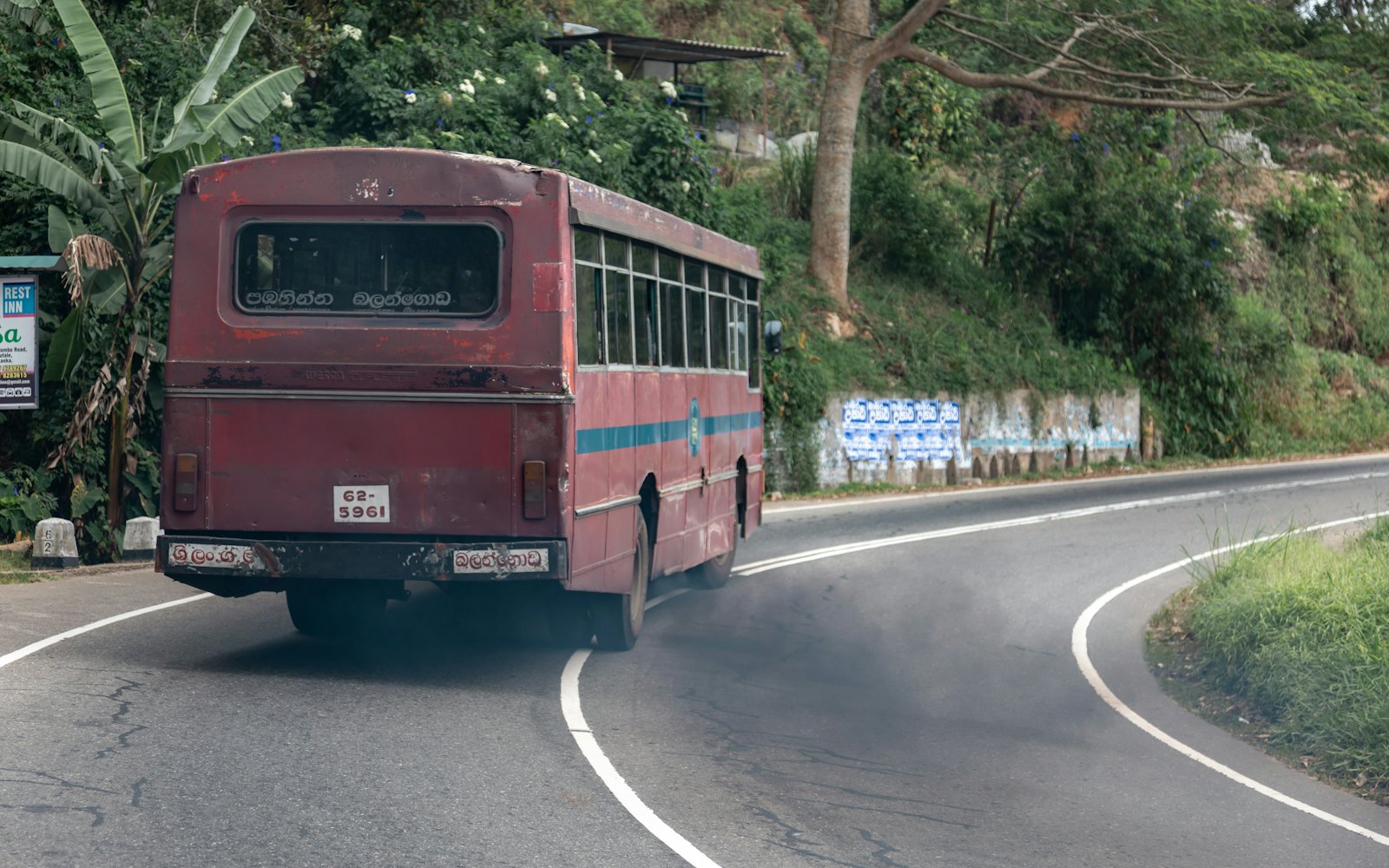 A red intercity bus rounding a bend on a Sri Lankan road
